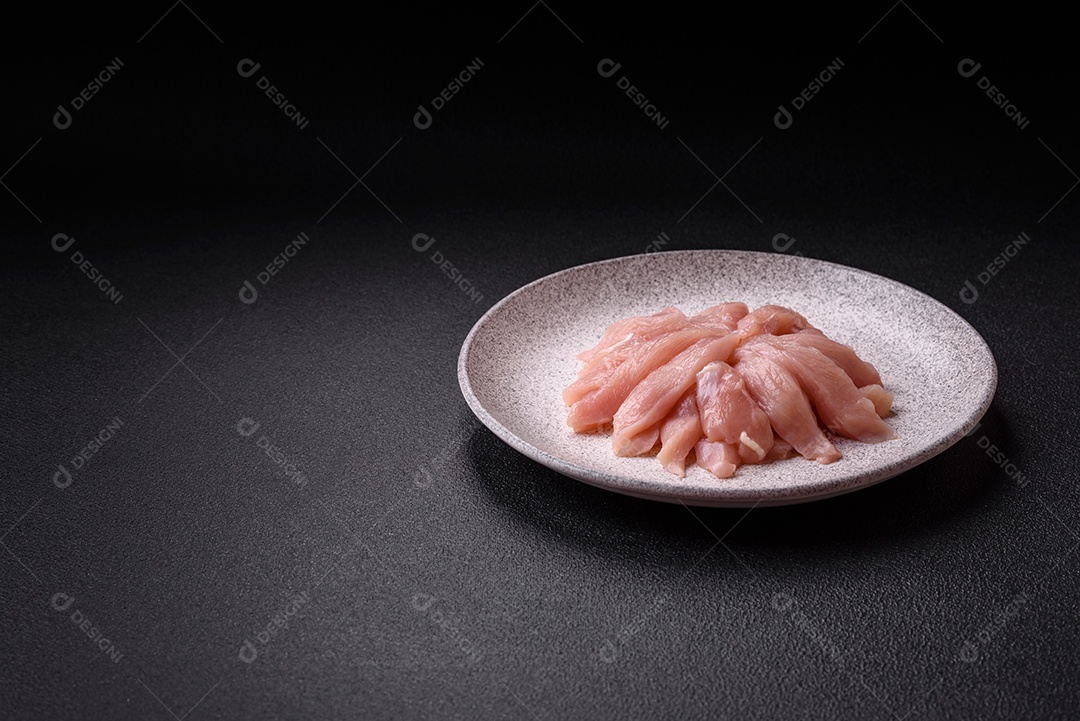 Fatias de frango cru ou filé de peru com sal, especiarias e ervas sobre um fundo escuro de concreto