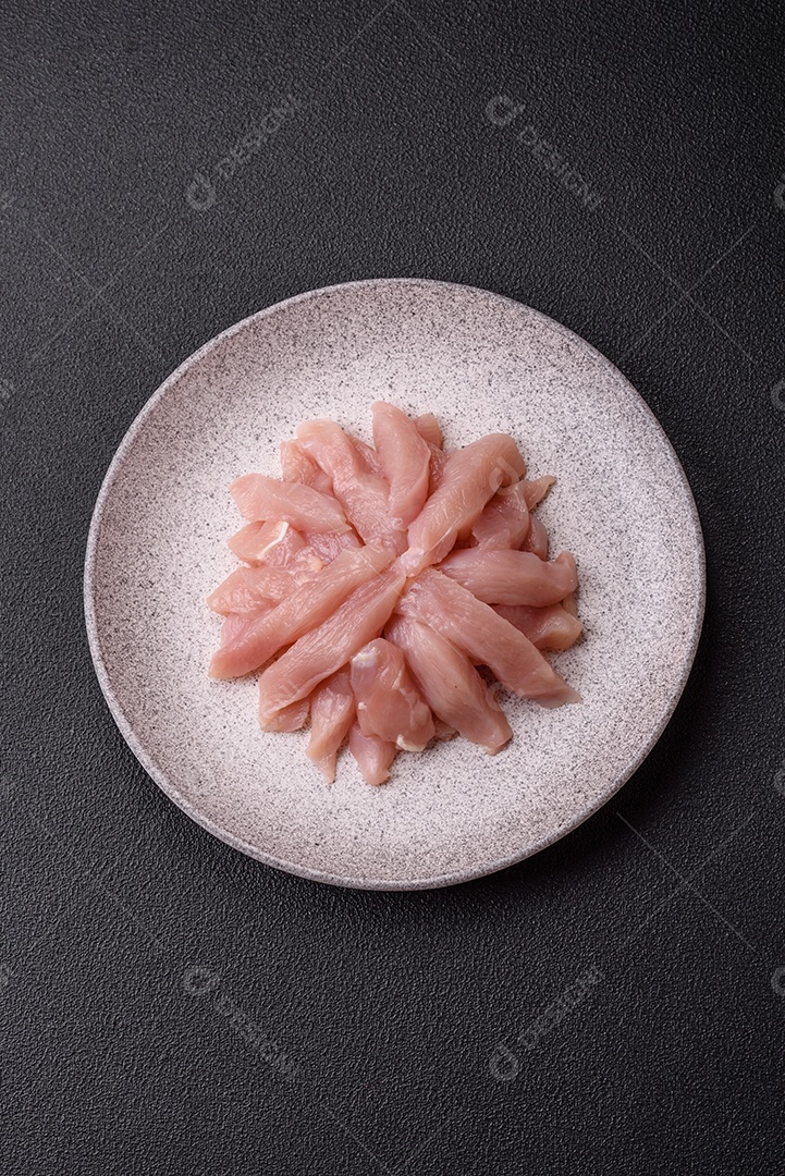 Fatias de frango cru ou filé de peru com sal, especiarias e ervas sobre um fundo escuro de concreto