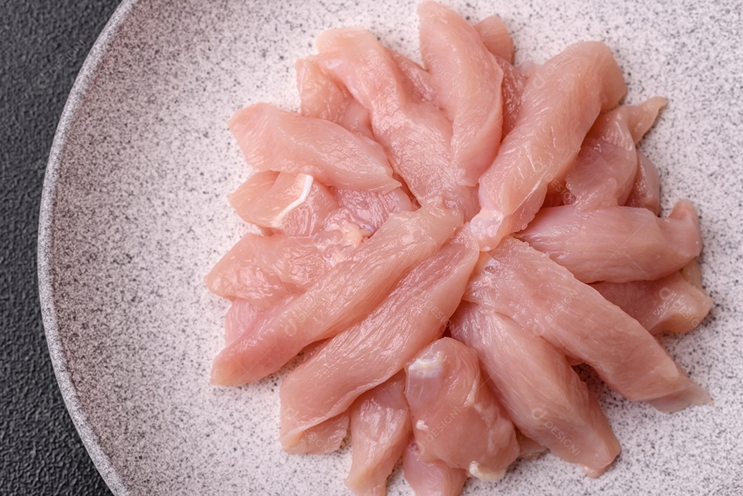 Fatias de frango cru ou filé de peru com sal, especiarias e ervas sobre um fundo escuro de concreto