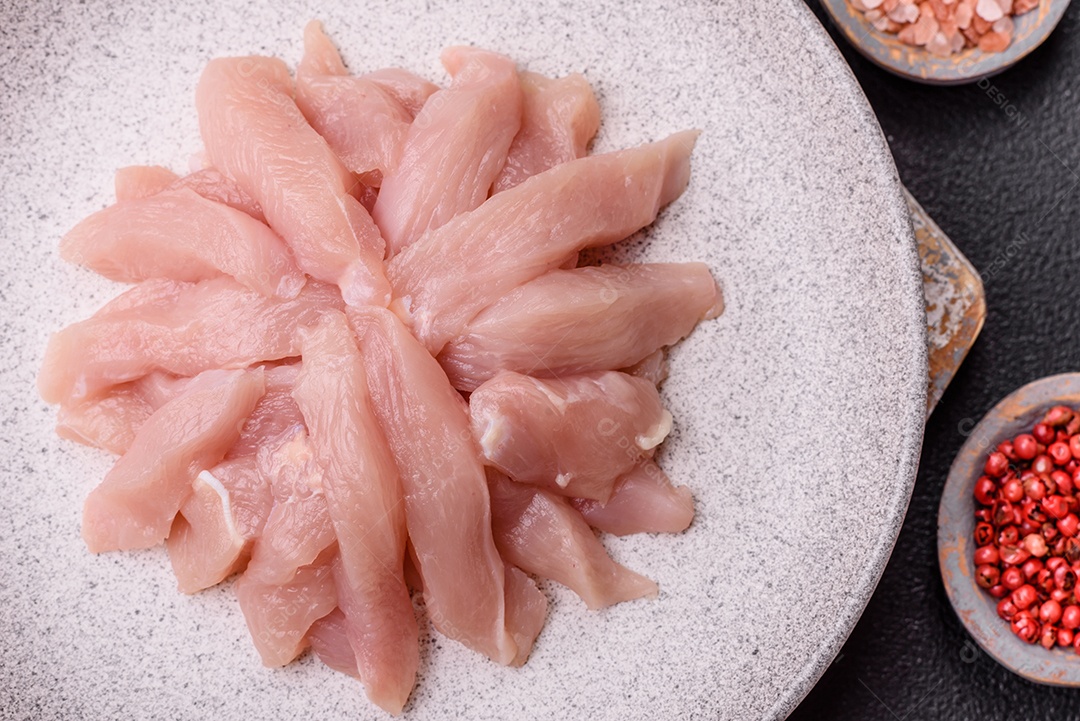 Fatias de frango cru ou filé de peru com sal, especiarias e ervas sobre um fundo escuro de concreto