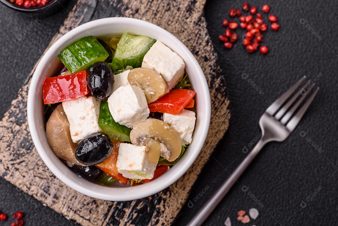 Deliciosa salada fresca e suculenta de pimentão, queijo, azeitonas, tomates, pepinos com sal e especiarias sobre um fundo escuro de concreto