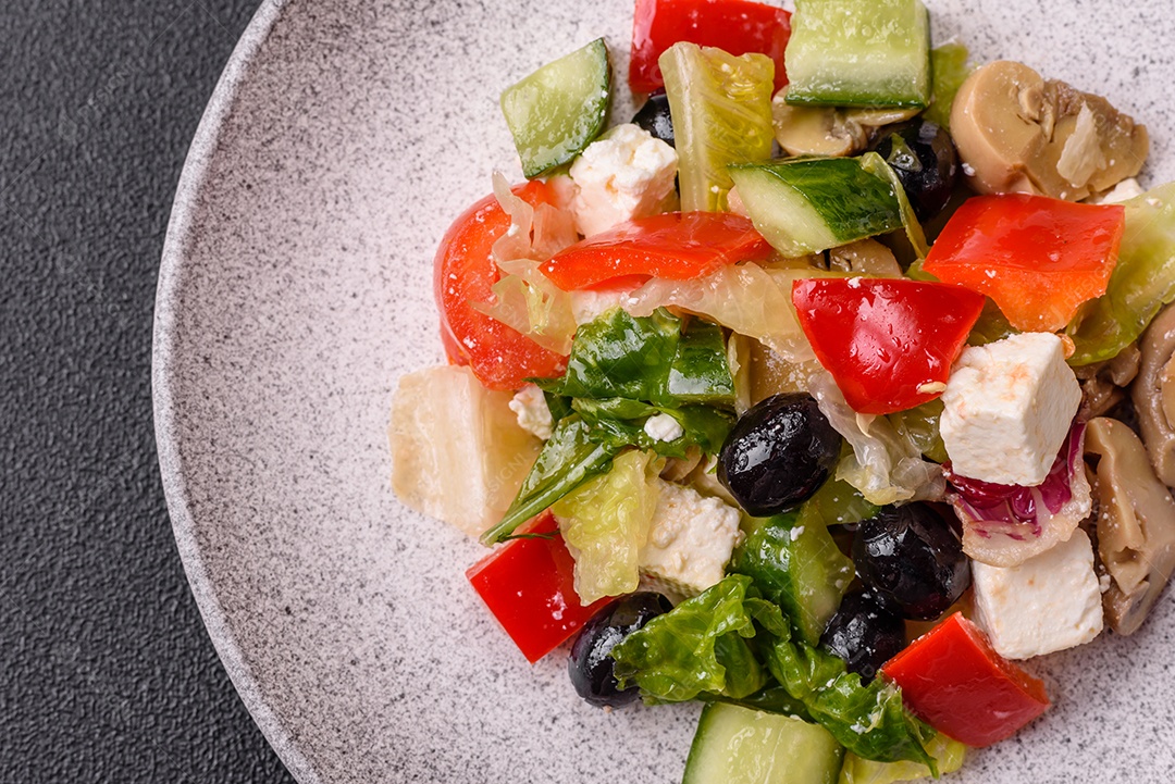 Deliciosa salada fresca e suculenta de pimentão, queijo, azeitonas, tomates, pepinos com sal e especiarias sobre um fundo escuro de concreto