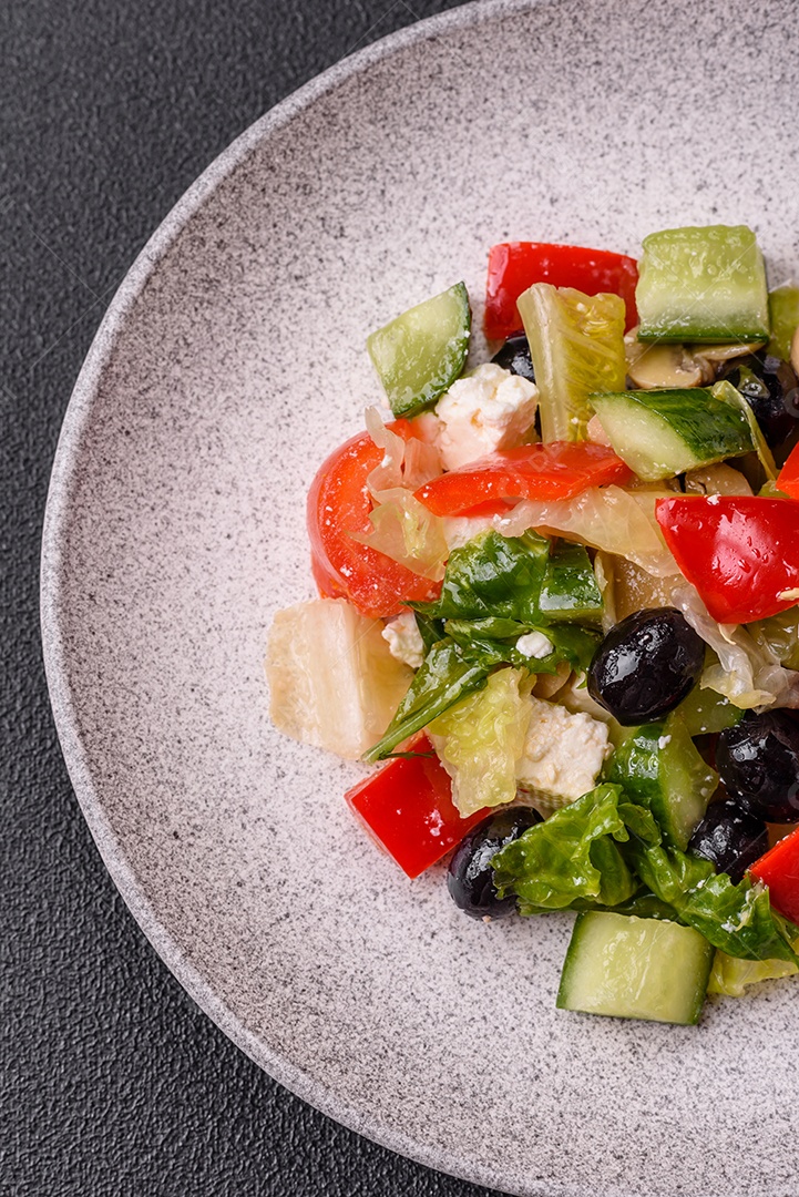 Deliciosa salada fresca e suculenta de pimentão, queijo, azeitonas, tomates, pepinos com sal e especiarias sobre um fundo escuro de concreto