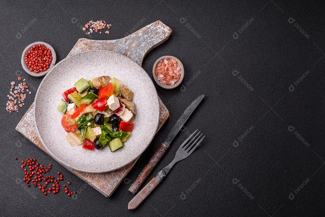 Deliciosa salada fresca e suculenta de pimentão, queijo, azeitonas, tomates, pepinos com sal e especiarias sobre um fundo escuro de concreto