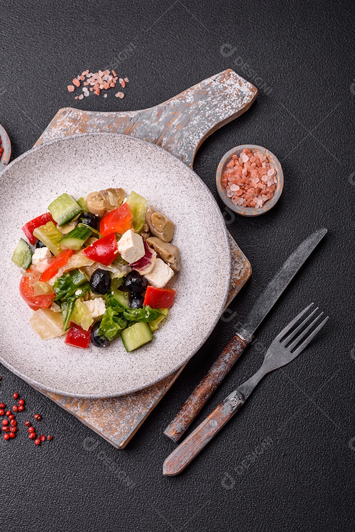 Deliciosa salada fresca e suculenta de pimentão, queijo, azeitonas, tomates, pepinos com sal e especiarias sobre um fundo escuro de concreto