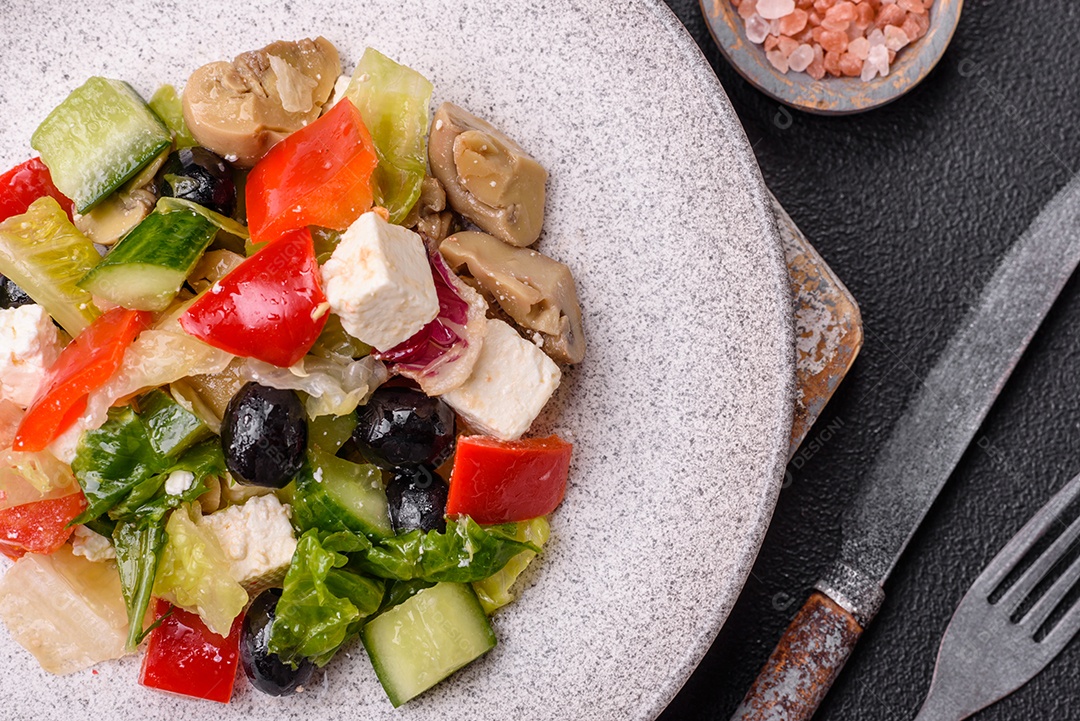 Deliciosa salada fresca e suculenta de pimentão, queijo, azeitonas, tomates, pepinos com sal e especiarias sobre um fundo escuro de concreto