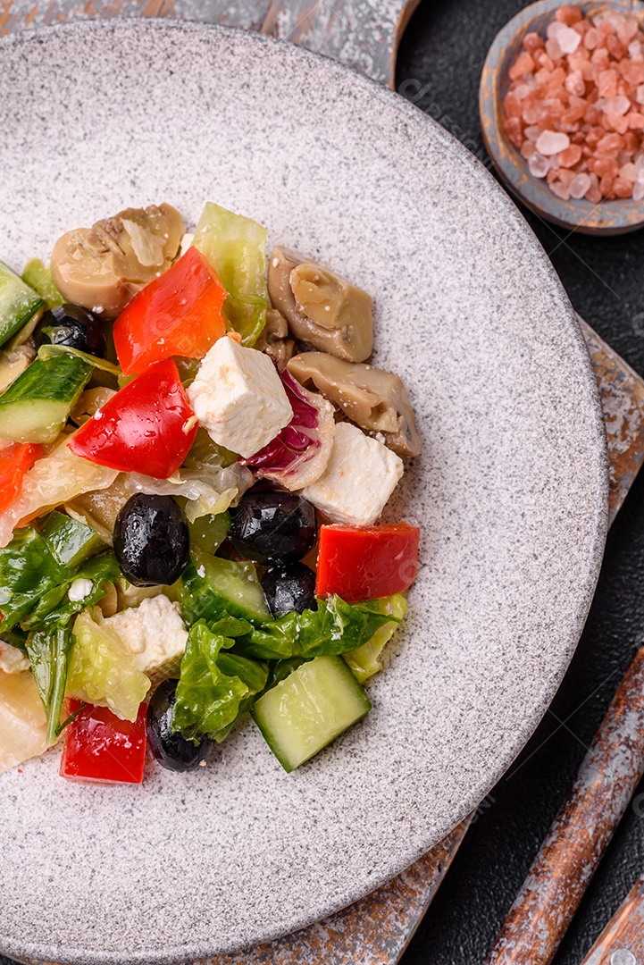 Deliciosa salada fresca e suculenta de pimentão, queijo, azeitonas, tomates, pepinos com sal e especiarias sobre um fundo escuro de concreto