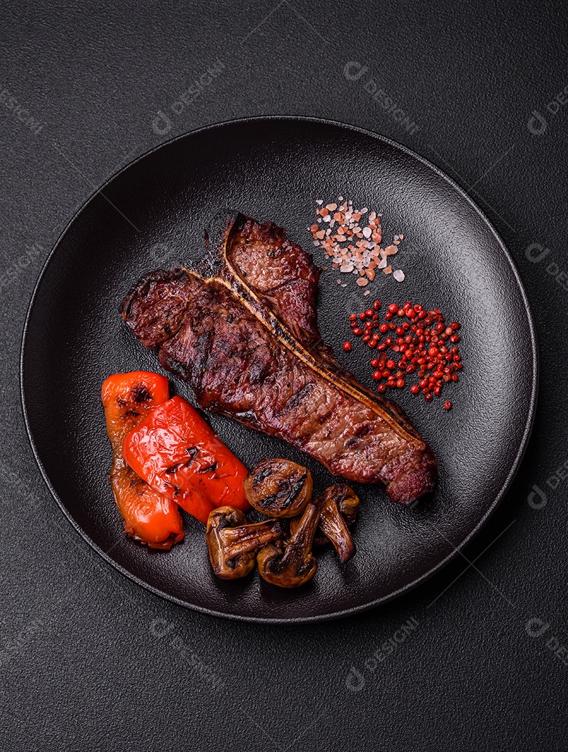Delicioso bife suculento com sal, especiarias e ervas sobre um fundo escuro de concreto