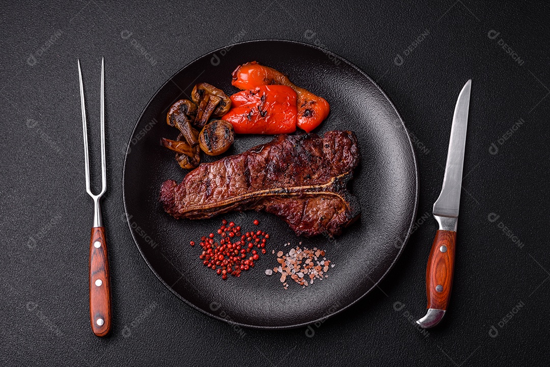 Delicioso bife suculento com sal, especiarias e ervas sobre um fundo escuro de concreto