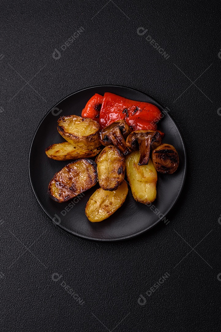 Deliciosos legumes grelhados, batatas, tomates, pimentões, berinjela com sal, especiarias e ervas em um fundo escuro de concreto