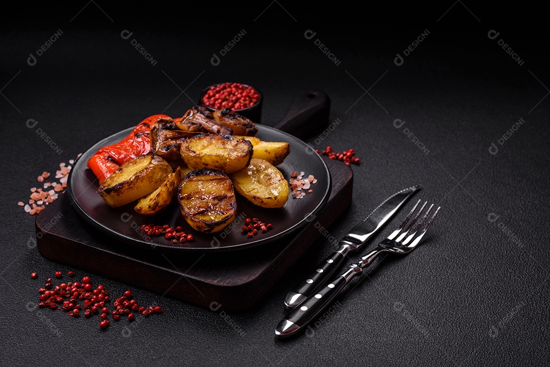 Deliciosos legumes grelhados, batatas, tomates, pimentões, berinjela com sal, especiarias e ervas em um fundo escuro de concreto