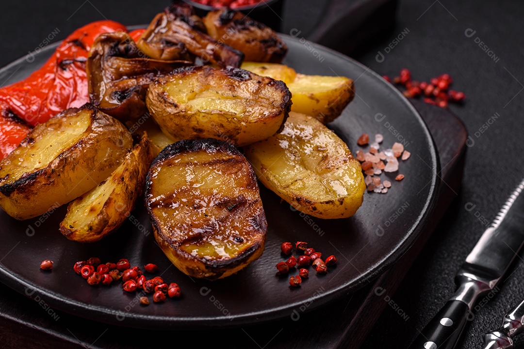 Deliciosos legumes grelhados, batatas, tomates, pimentões, berinjela com sal, especiarias e ervas em um fundo escuro de concreto