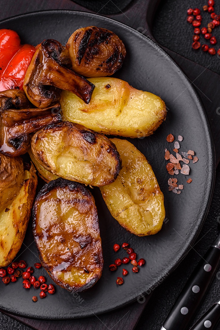 Deliciosos legumes grelhados, batatas, tomates, pimentões, berinjela com sal, especiarias e ervas em um fundo escuro de concreto
