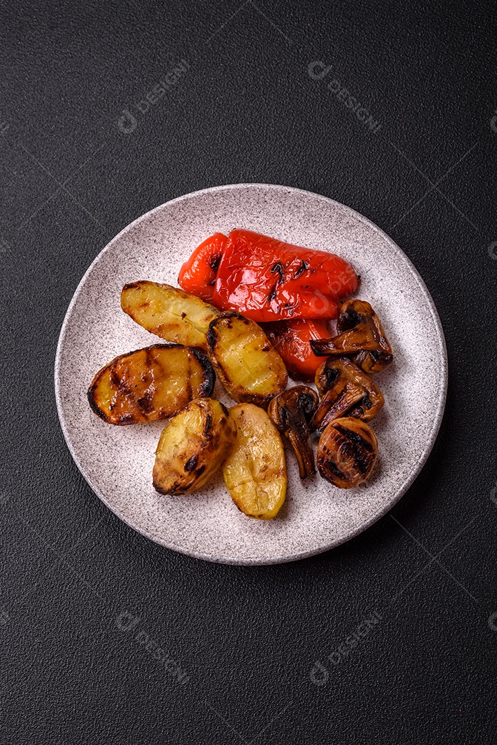 Deliciosos legumes grelhados, batatas, tomates, pimentões, berinjela com sal, especiarias e ervas em um fundo escuro de concreto