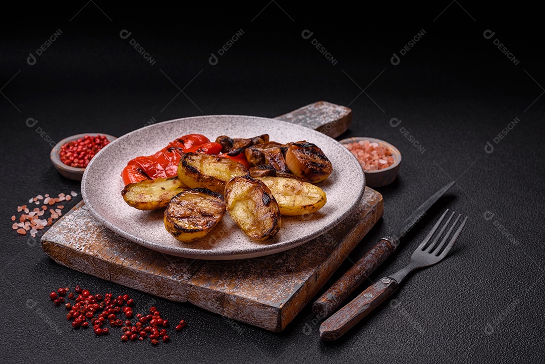 Deliciosos legumes grelhados, batatas, tomates, pimentões, berinjela com sal, especiarias e ervas em um fundo escuro de concreto