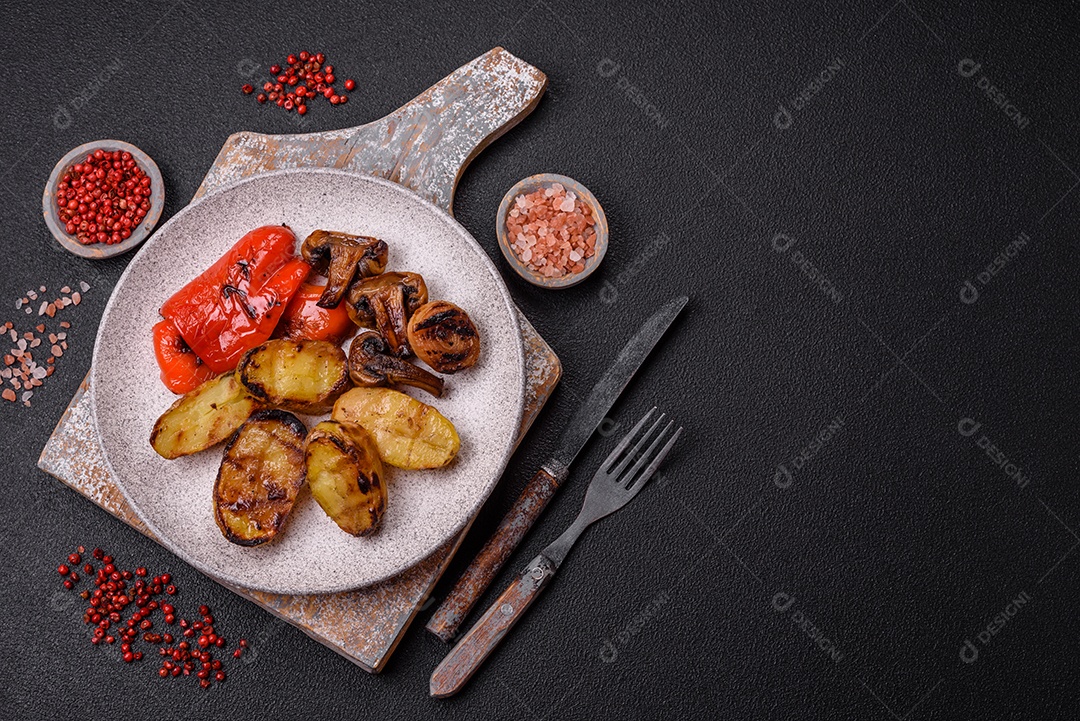 Deliciosos legumes grelhados, batatas, tomates, pimentões, berinjela com sal, especiarias e ervas em um fundo escuro de concreto