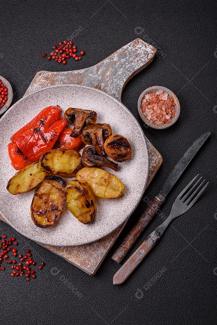 Deliciosos legumes grelhados, batatas, tomates, pimentões, berinjela com sal, especiarias e ervas em um fundo escuro de concreto