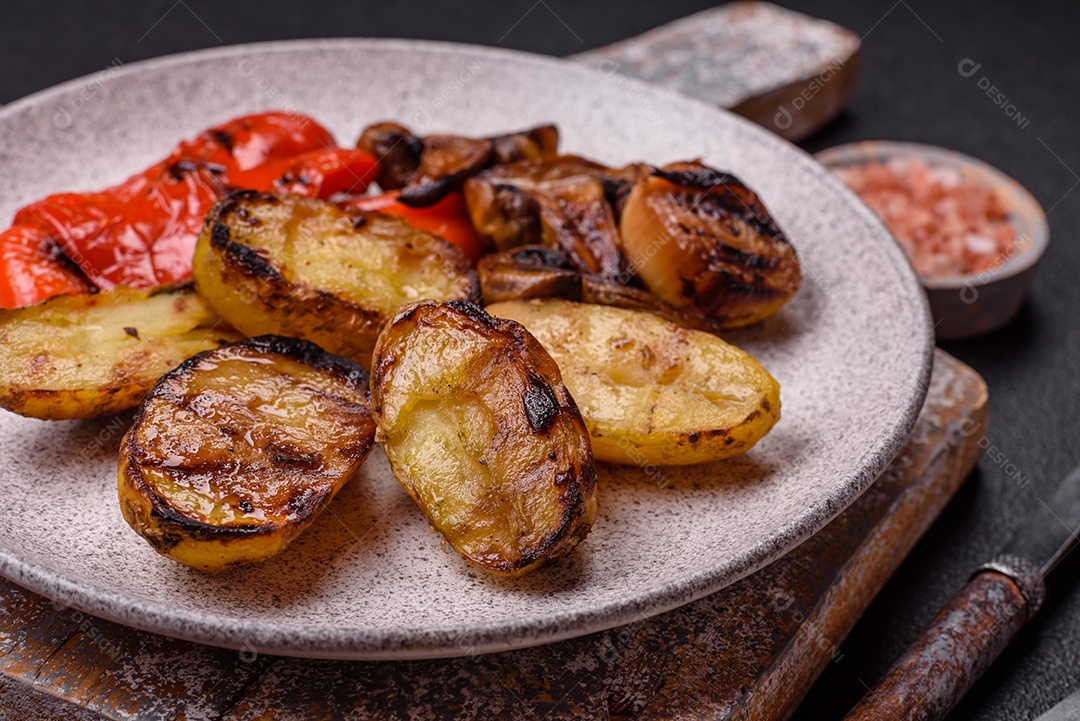 Deliciosos legumes grelhados, batatas, tomates, pimentões, berinjela com sal, especiarias e ervas em um fundo escuro de concreto