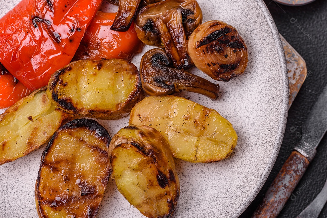 Deliciosos legumes grelhados, batatas, tomates, pimentões, berinjela com sal, especiarias e ervas em um fundo escuro de concreto