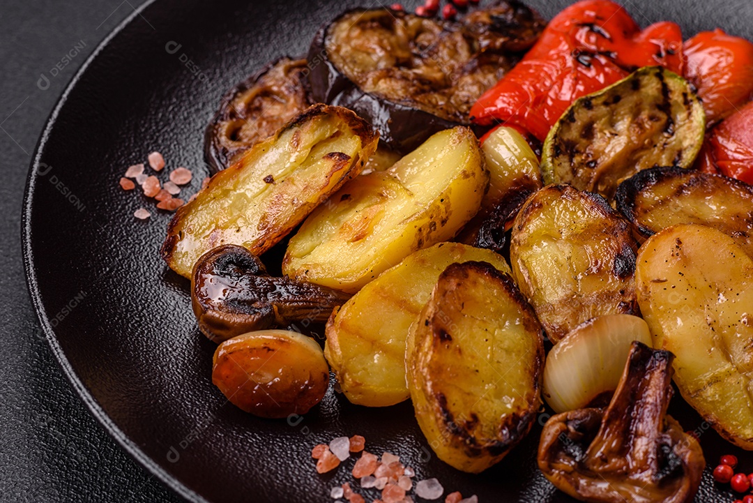 Deliciosos legumes grelhados, batatas, tomates, pimentões, berinjela com sal, especiarias e ervas em um fundo escuro de concreto