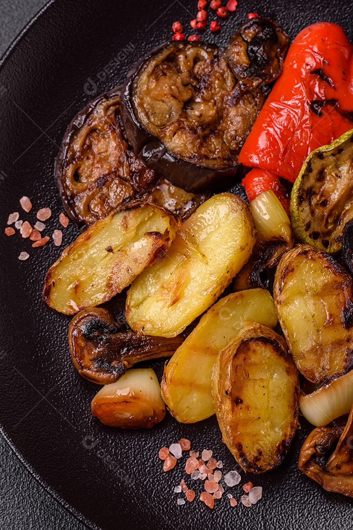 Deliciosos legumes grelhados, batatas, tomates, pimentões, berinjela com sal, especiarias e ervas em um fundo escuro de concreto