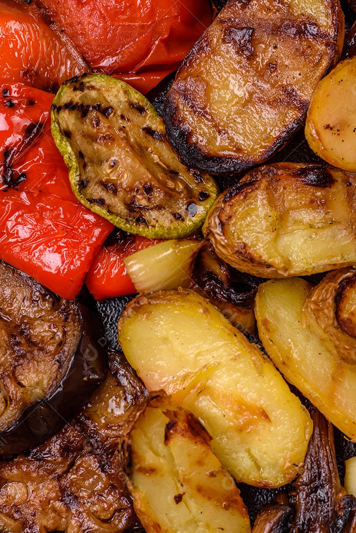 Deliciosos legumes grelhados, batatas, tomates, pimentões, berinjela com sal, especiarias e ervas em um fundo escuro de concreto
