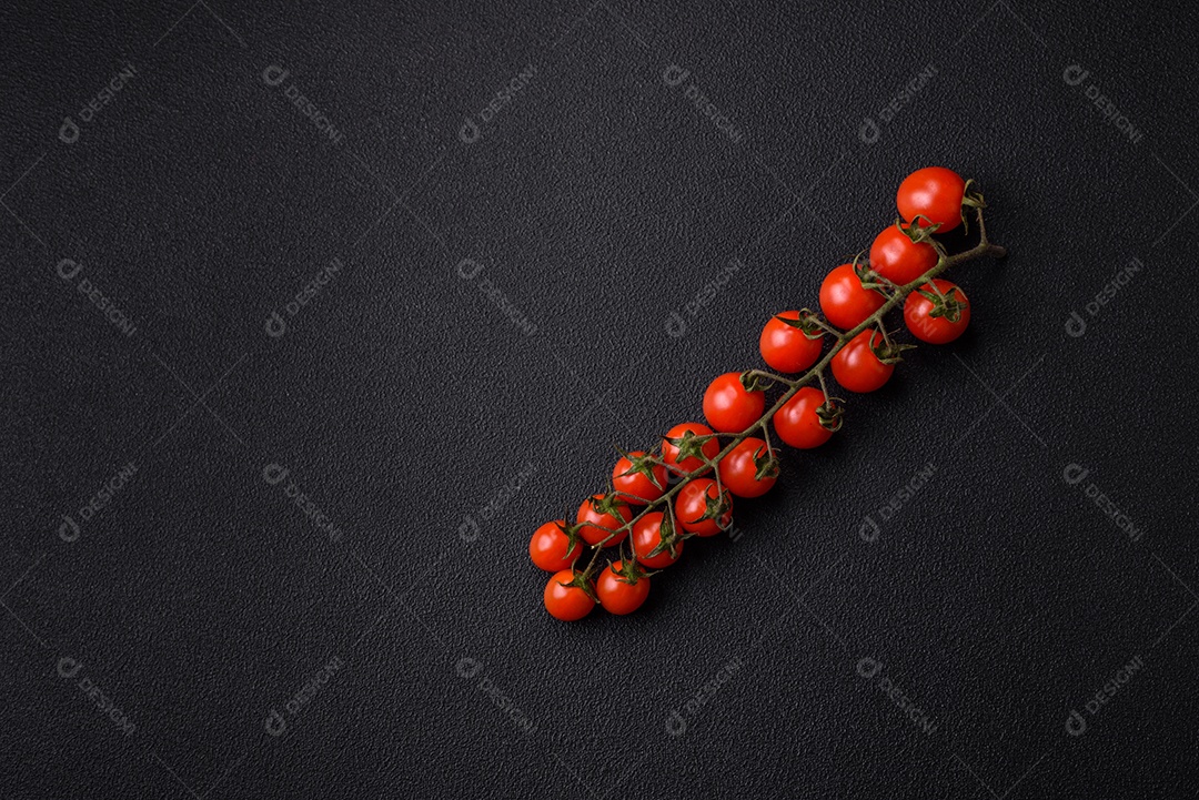 Um raminho de tomate cereja vermelho maduro como ingrediente para cozinhar em casa sobre um fundo preto de concreto