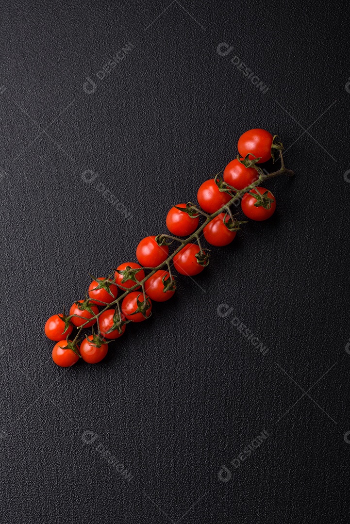 Um raminho de tomate cereja vermelho maduro como ingrediente para cozinhar em casa sobre um fundo preto de concreto