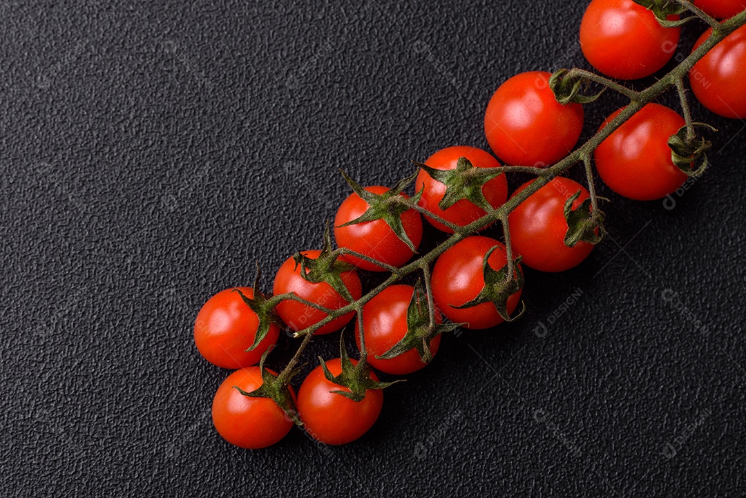 Um raminho de tomate cereja vermelho maduro como ingrediente para cozinhar em casa sobre um fundo preto de concreto