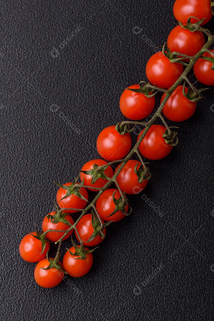 Um raminho de tomate cereja vermelho maduro como ingrediente para cozinhar em casa sobre um fundo preto de concreto