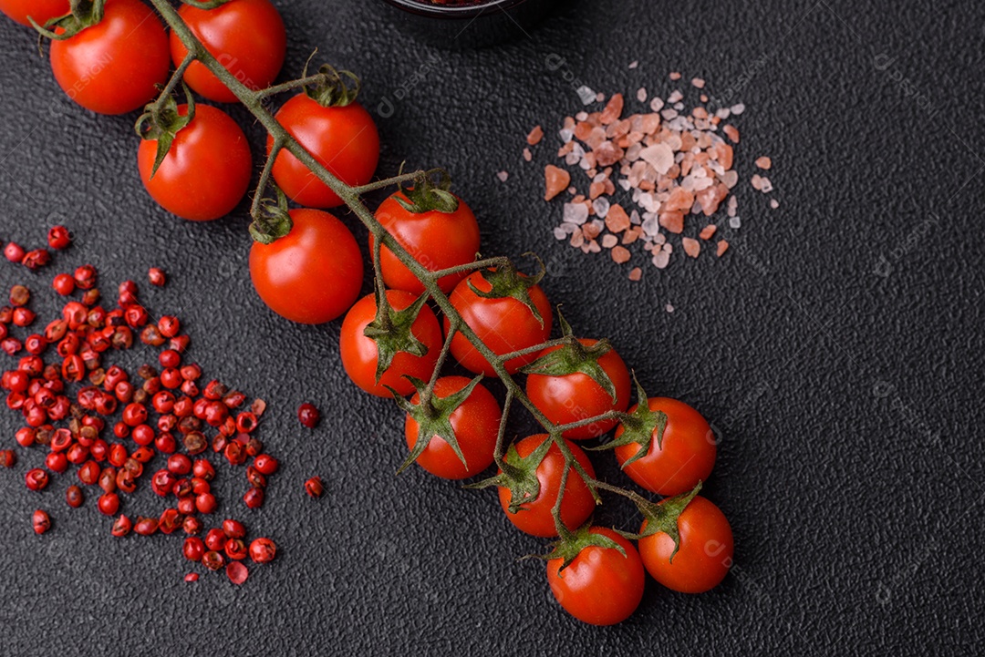 Um raminho de tomate cereja vermelho maduro como ingrediente para cozinhar em casa sobre um fundo preto de concreto