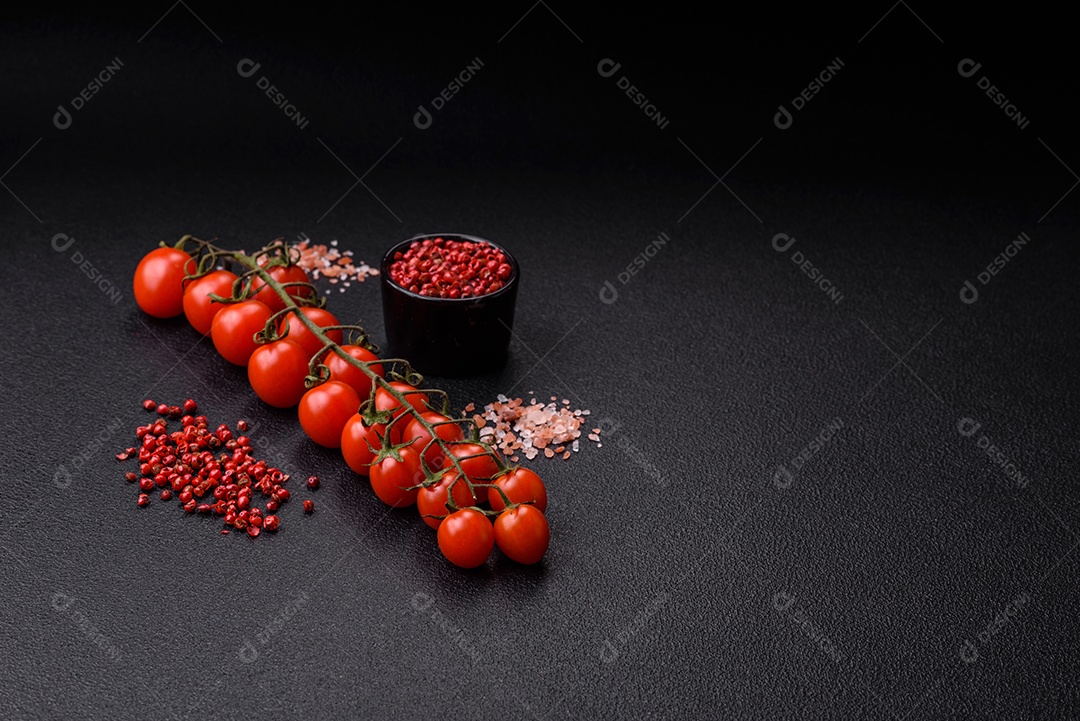 Um raminho de tomate cereja vermelho maduro como ingrediente para cozinhar em casa sobre um fundo preto de concreto