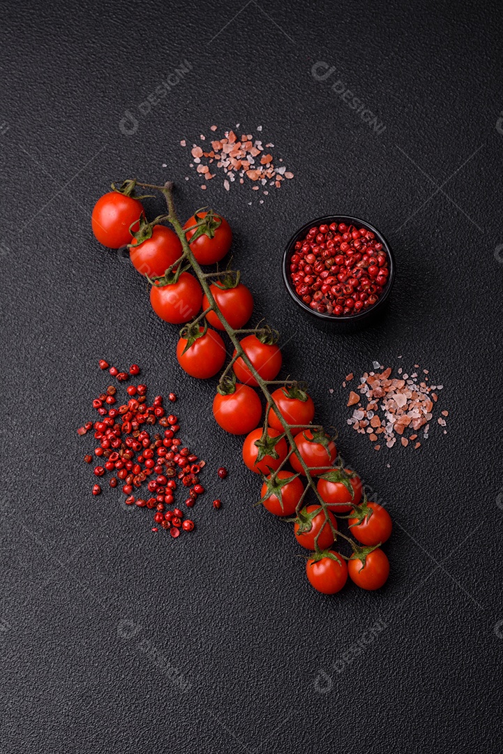 Um raminho de tomate cereja vermelho maduro como ingrediente para cozinhar em casa sobre um fundo preto de concreto