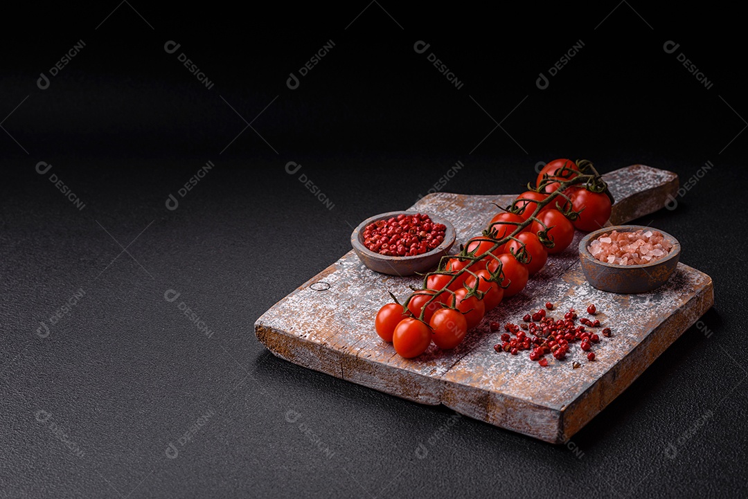 Um raminho de tomate cereja vermelho maduro como ingrediente para cozinhar em casa sobre um fundo preto de concreto