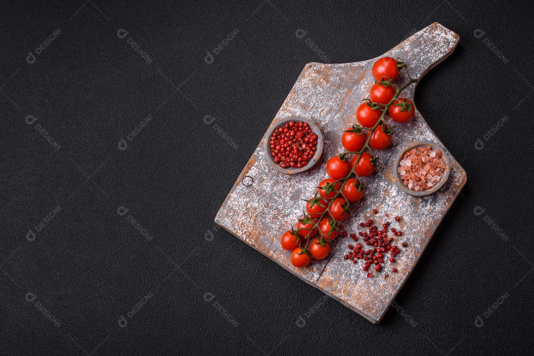 Um raminho de tomate cereja vermelho maduro como ingrediente para cozinhar em casa sobre um fundo preto de concreto