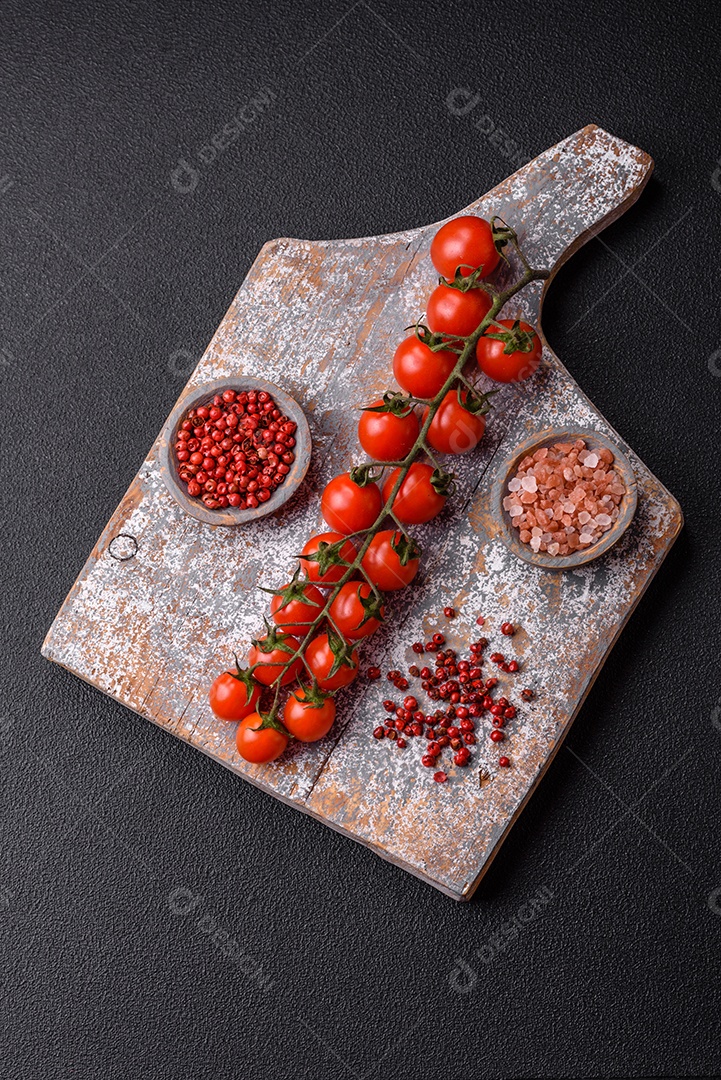 Um raminho de tomate cereja vermelho maduro como ingrediente para cozinhar em casa sobre um fundo preto de concreto
