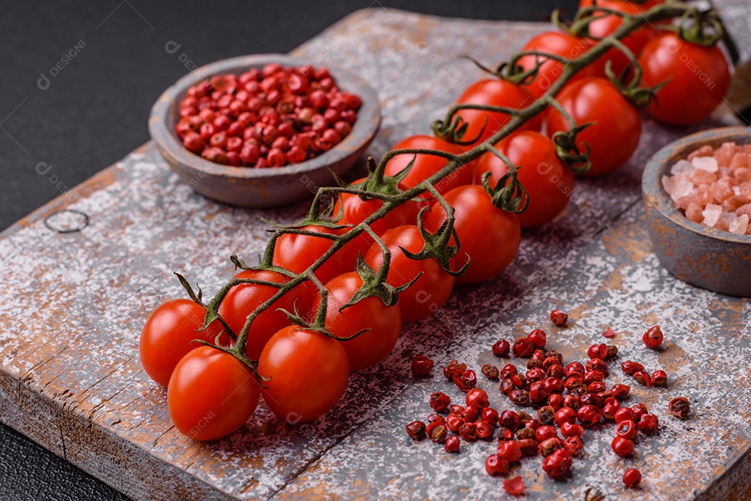 Um raminho de tomate cereja vermelho maduro como ingrediente para cozinhar em casa sobre um fundo preto de concreto