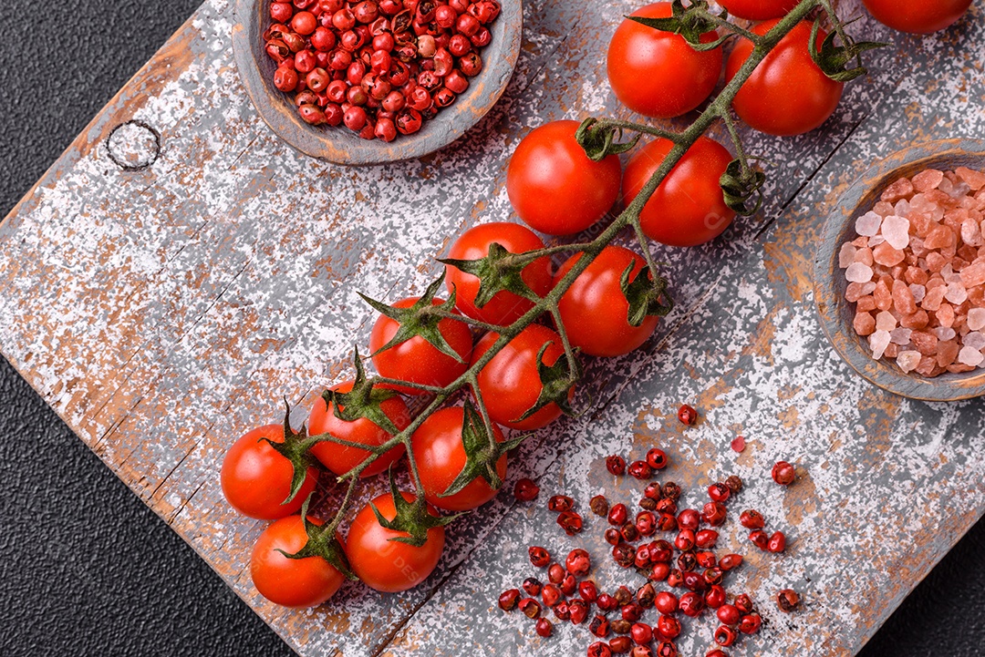 Um raminho de tomate cereja vermelho maduro como ingrediente para cozinhar em casa sobre um fundo preto de concret