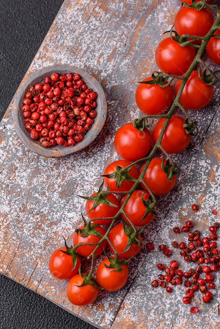 Um raminho de tomate cereja vermelho maduro como ingrediente para cozinhar em casa sobre um fundo preto de concreto