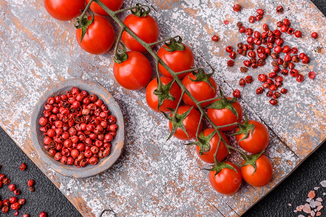 Um raminho de tomate cereja vermelho maduro como ingrediente para cozinhar em casa sobre um fundo preto de concreto