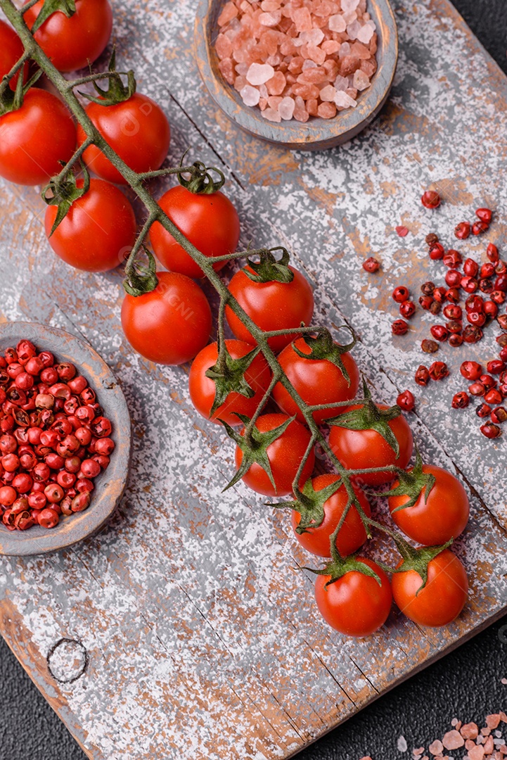 Um raminho de tomate cereja vermelho maduro como ingrediente para cozinhar em casa sobre um fundo preto de concreto