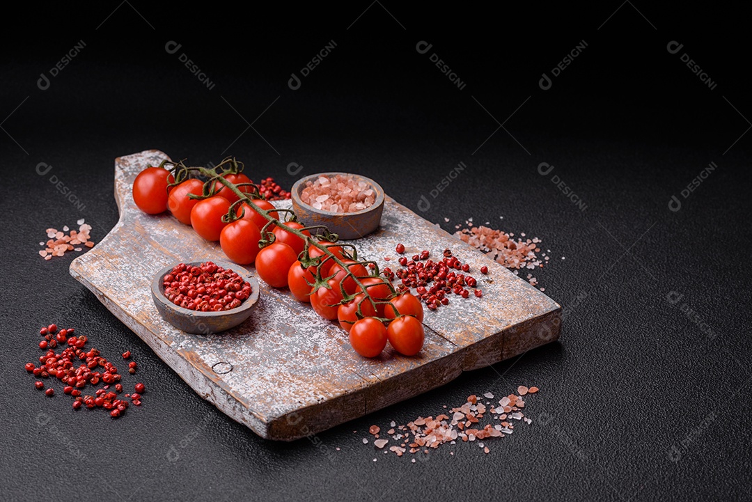 Um raminho de tomate cereja vermelho maduro como ingrediente para cozinhar em casa sobre um fundo preto de concreto