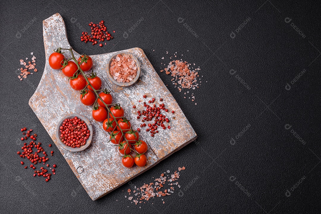 Um raminho de tomate cereja vermelho maduro como ingrediente para cozinhar em casa sobre um fundo preto de concreto