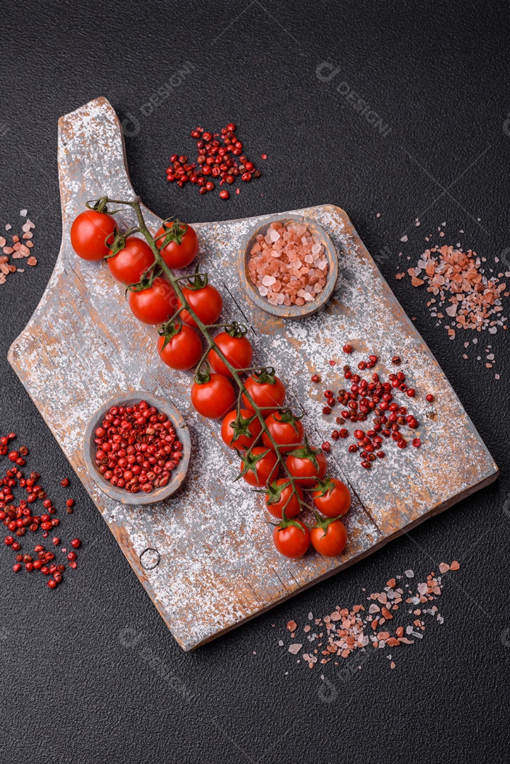 Um raminho de tomate cereja vermelho maduro como ingrediente para cozinhar em casa sobre um fundo preto de concreto