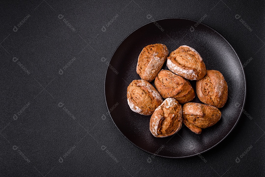 Pãezinhos de pão fresco com sal, especiarias, sementes e grãos sobre fundo escuro