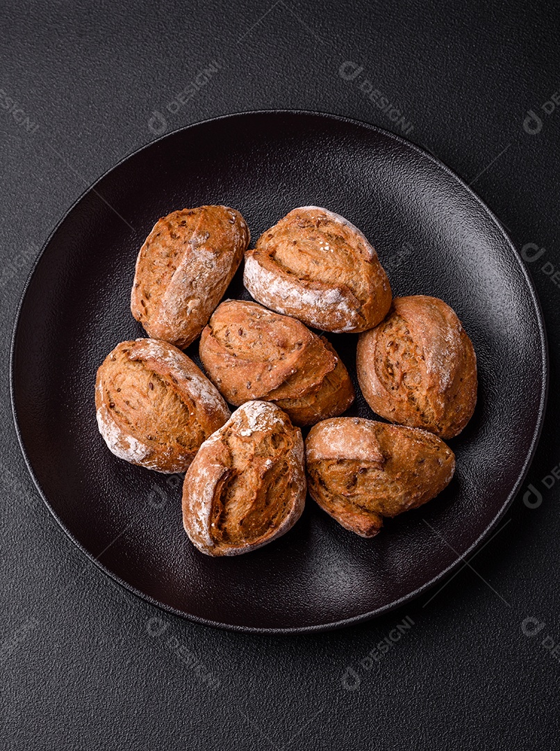 Pãezinhos de pão fresco com sal, especiarias, sementes e grãos sobre fundo escuro