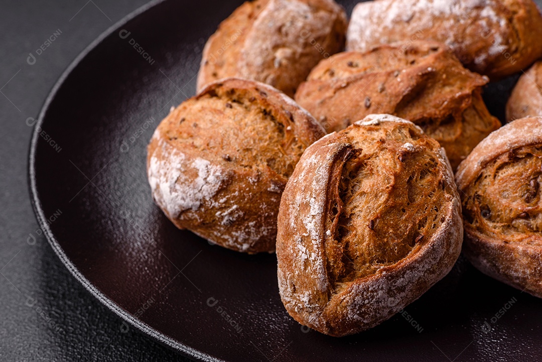 Pãezinhos de pão fresco com sal, especiarias, sementes e grãos sobre fundo escuro
