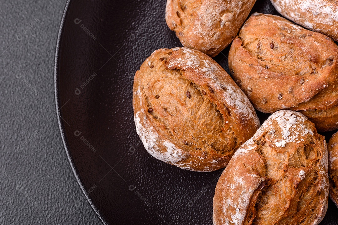 Pãezinhos de pão fresco com sal, especiarias, sementes e grãos sobre fundo escuro