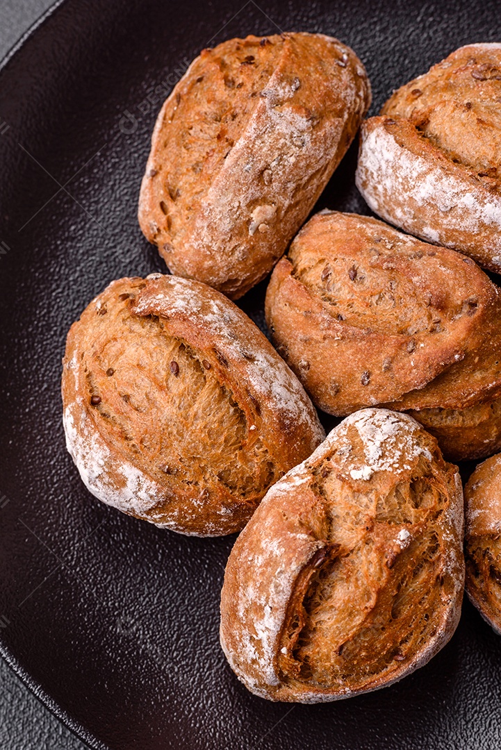 Pãezinhos de pão fresco com sal, especiarias, sementes e grãos sobre fundo escuro