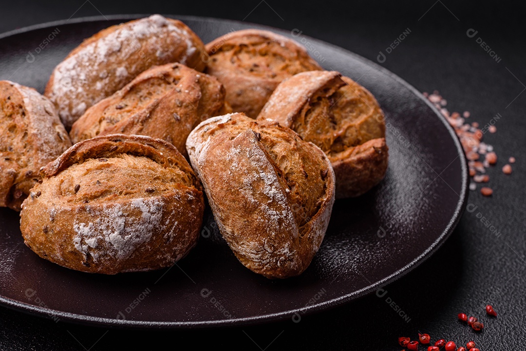 Pãezinhos de pão fresco com sal, especiarias, sementes e grãos sobre fundo escuro